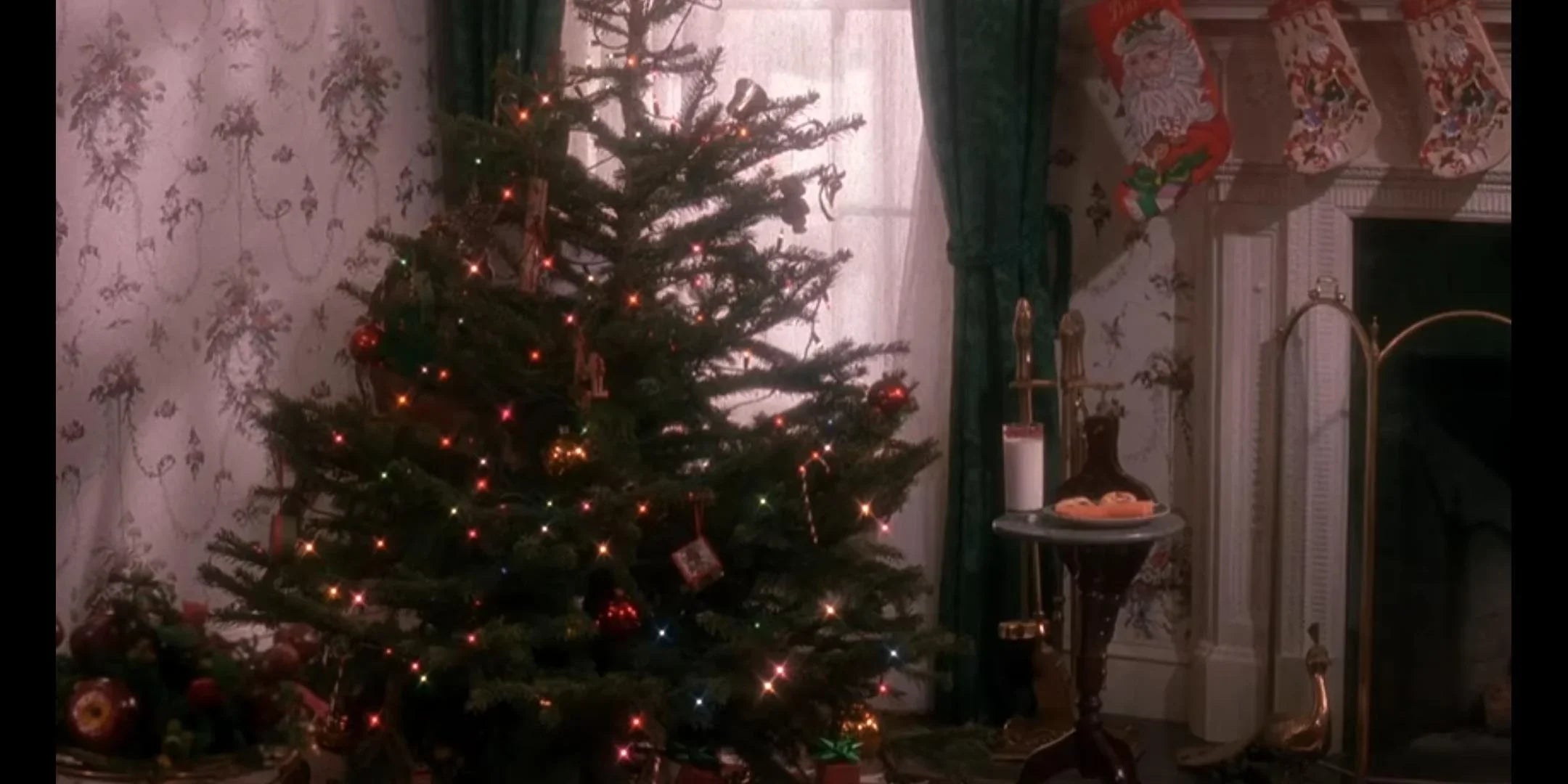 A cozy living room decorated for Christmas, with a lit tree, stockings on the fireplace, garlands, and a young boy in a green robe sitting on a couch, gazing at the festive decorations.