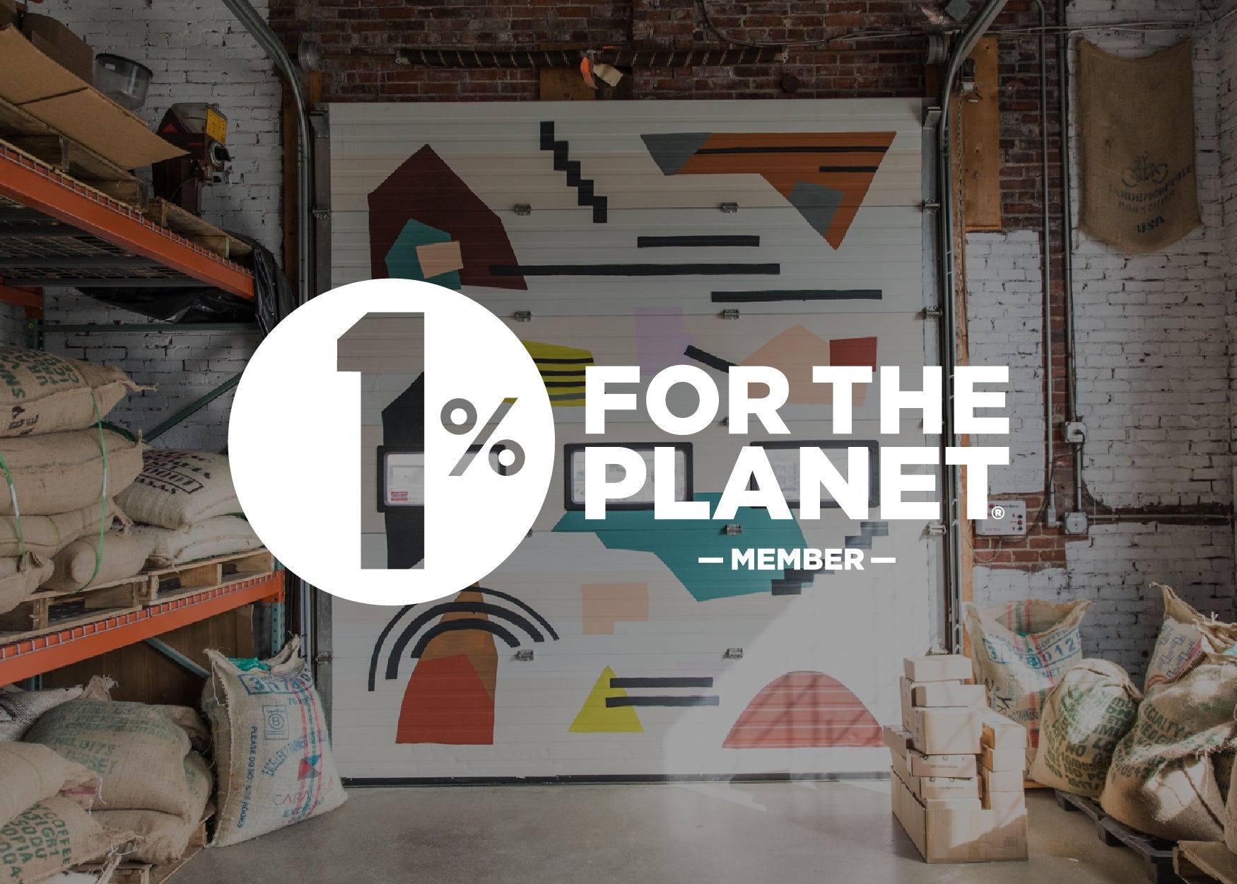 An industrial warehouse with a garage door featuring a modern, geometric mural. in the foreground, there are burlap sacks and wooden crates. a logo reads "1% for the planet - member.