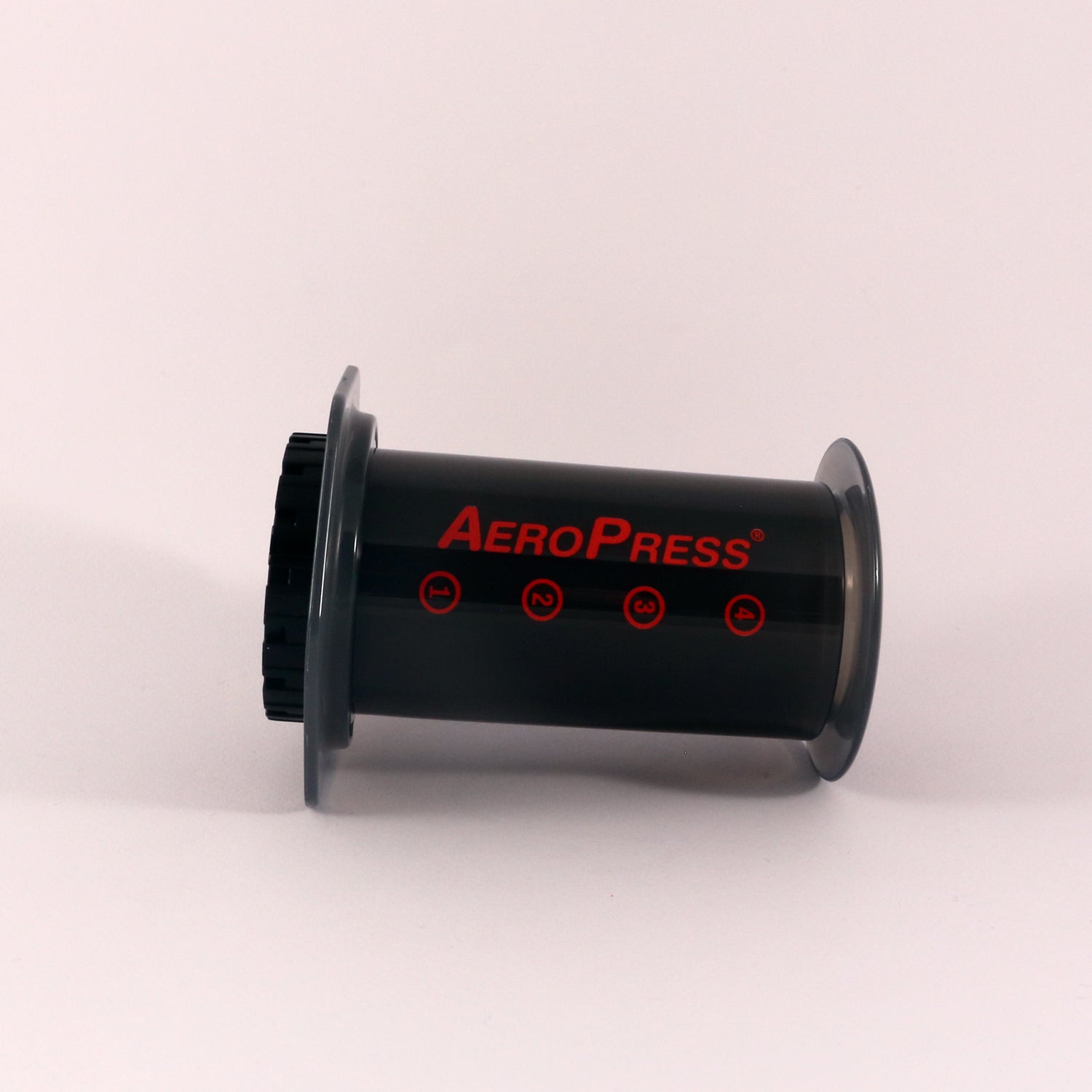 An Tandem Aeropress coffee maker, branded as the world's greatest, on a gray background. It features a black cylindrical body adorned with the logo and measurement markers in red and is assembled and ready for.