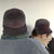 Two people wearing custom Tandem Coffee Roasters corduroy tandem hats with embroidered bicycle designs, viewed from the back. One hat is dark gray, the other lighter, both facing a light grey background.