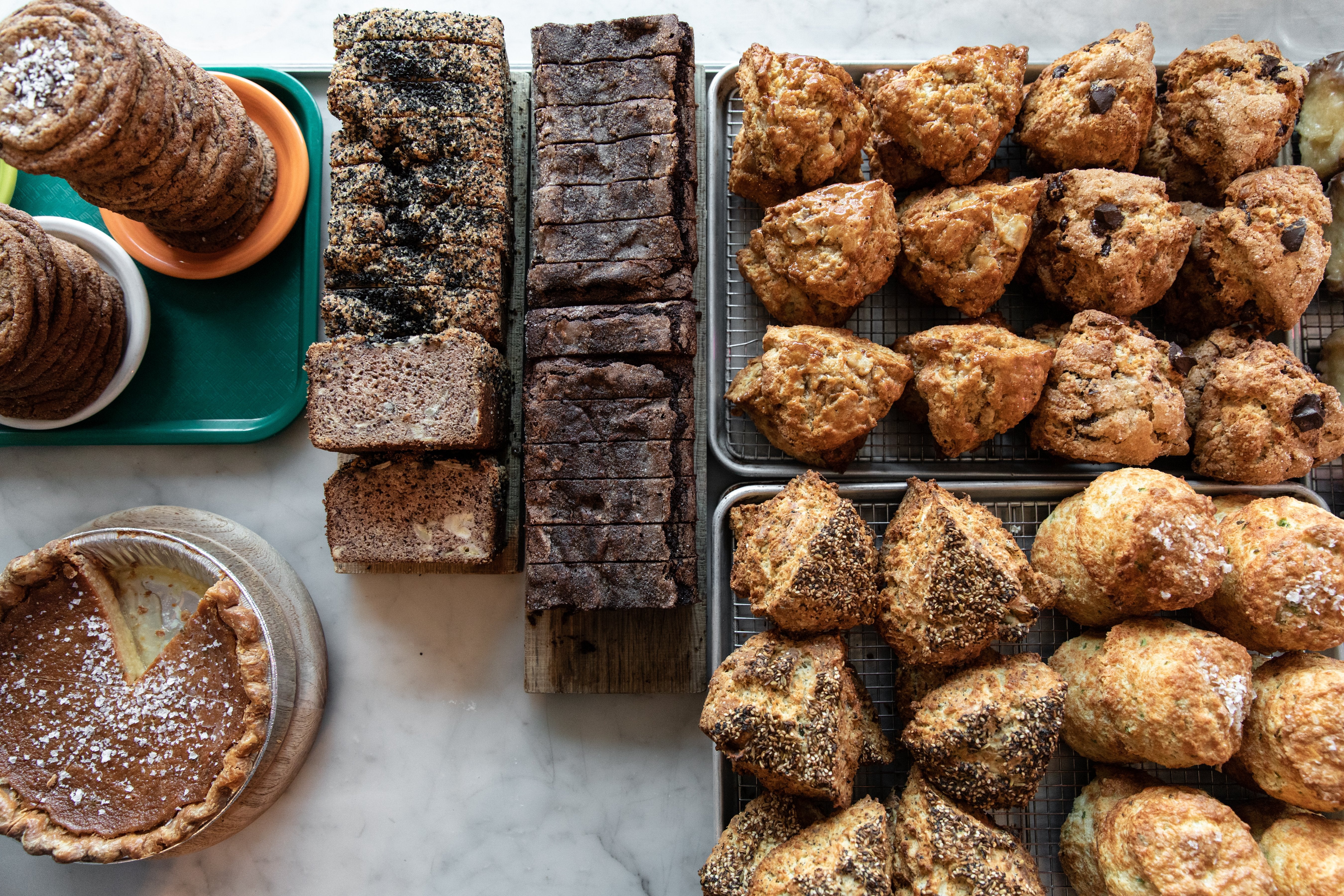 An assortment of baked goods displayed on a marble counter, including slices of brown bread, chocolate bread, scones, and a pumpkin pie.