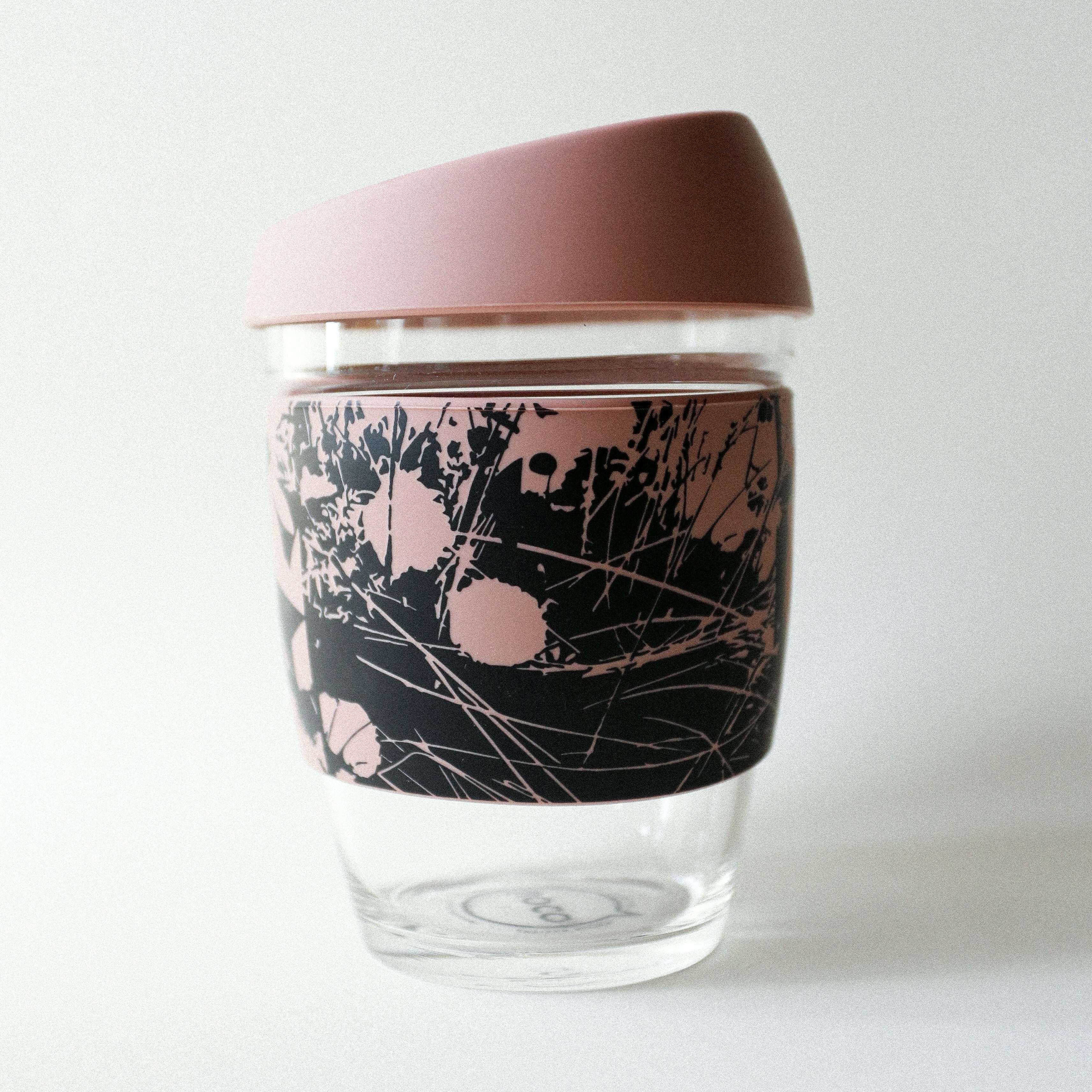 The Tandem x NUUFORM Joco Cup by vendor-unknown is a plastic-free, reusable borosilicate glass cup with a pink lid and a pink-and-black abstract floral silicone band, shown on a plain white background.