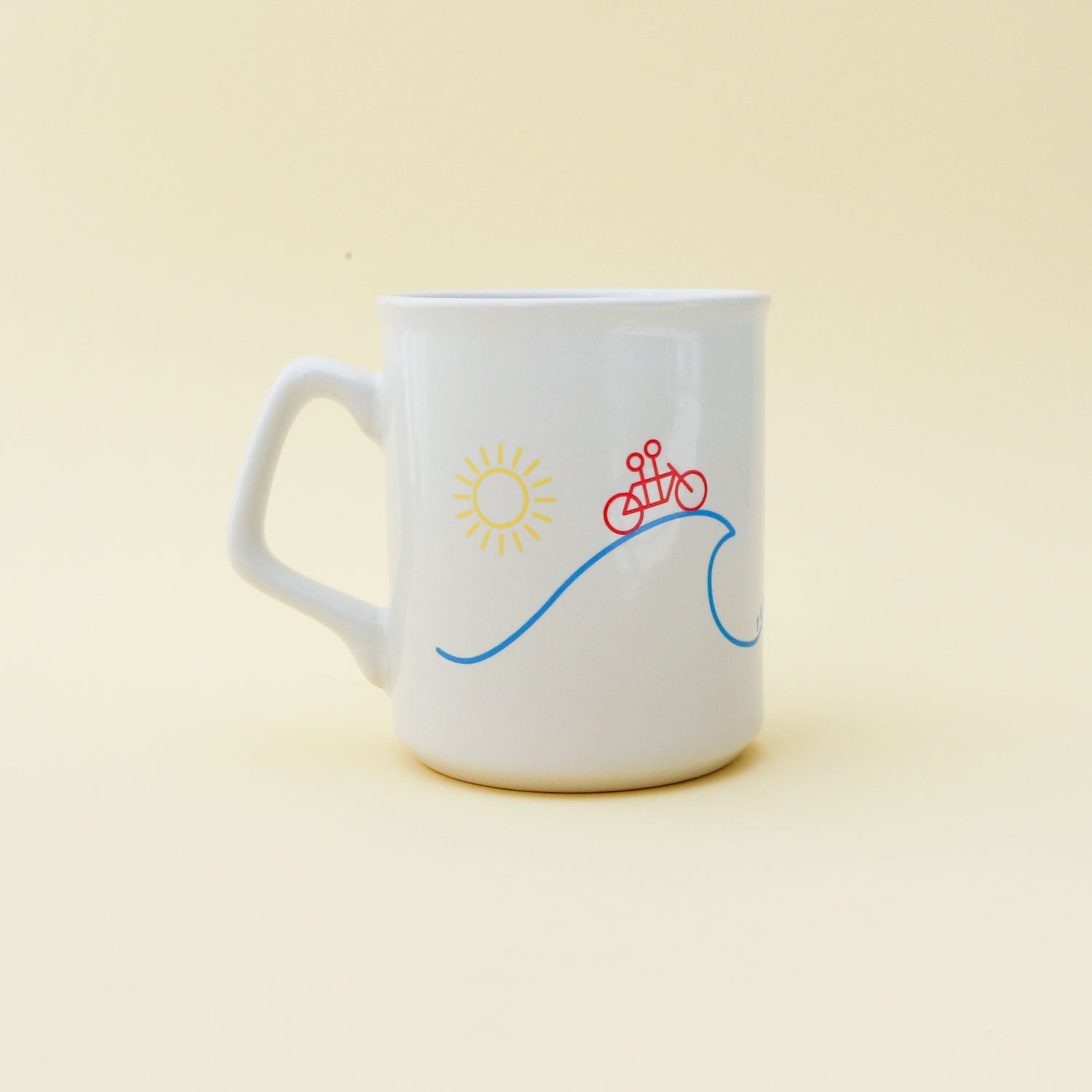 A classic white 11oz Sunshine Mug with a sun and a red bicycle design above a blue wave, set against a pale yellow background by Tandem Coffee Roasters.