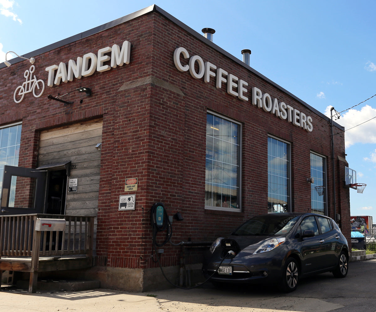 A brick building with a sign reading "tandem coffee roasters" and a bicycle symbol, with a blue car parked in front.