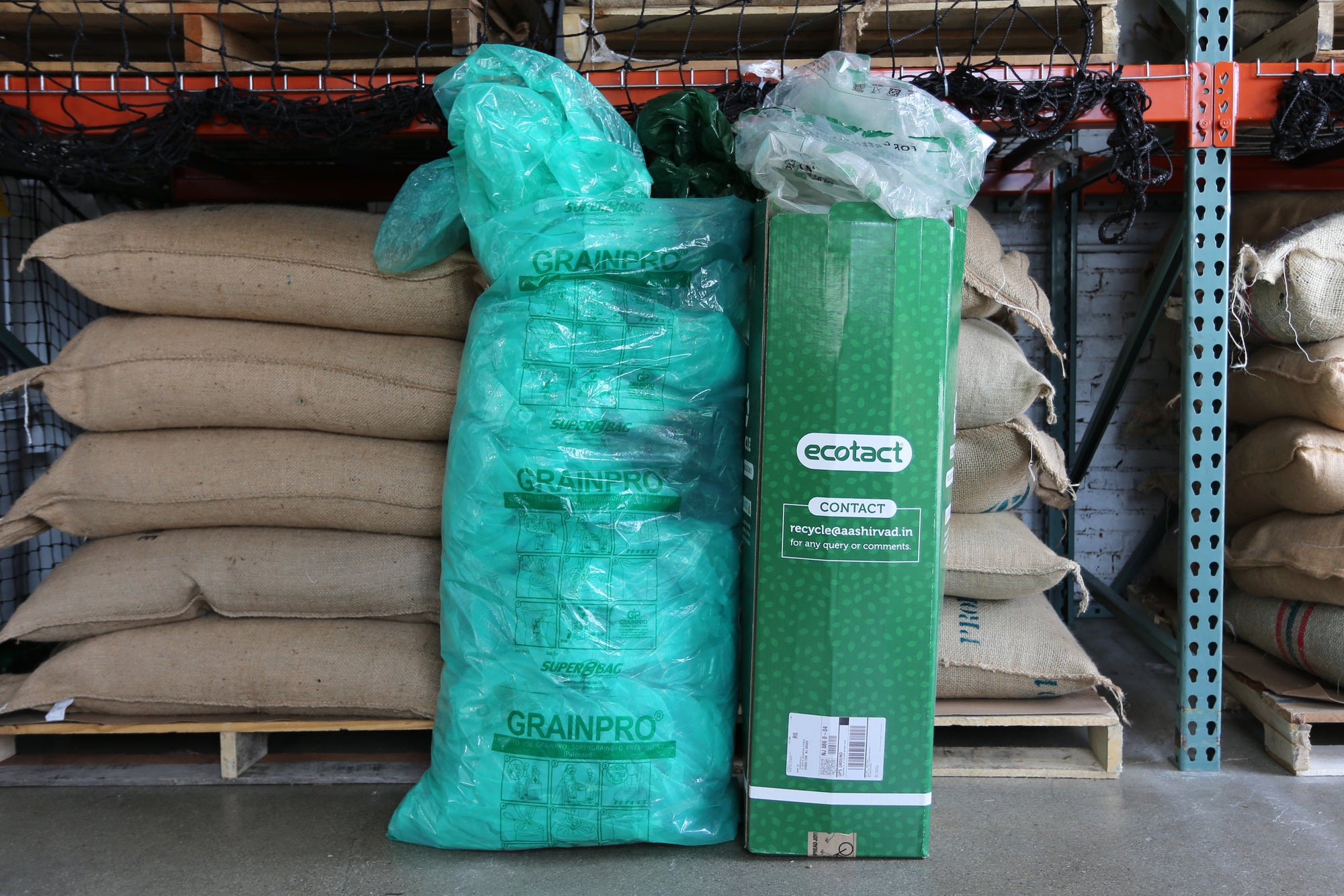 Stacks of grainpro bags and a box labeled "ecotact" in a warehouse setting, used for storing agricultural products to preserve freshness and prevent spoilage.