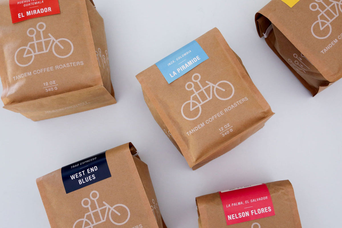 Several neatly arranged coffee bags from tandem coffee roasters, each with distinct labels like "el mirador," "la pirámide," "west end blues," and "nelson flores," featuring simple bicycle graphics.
