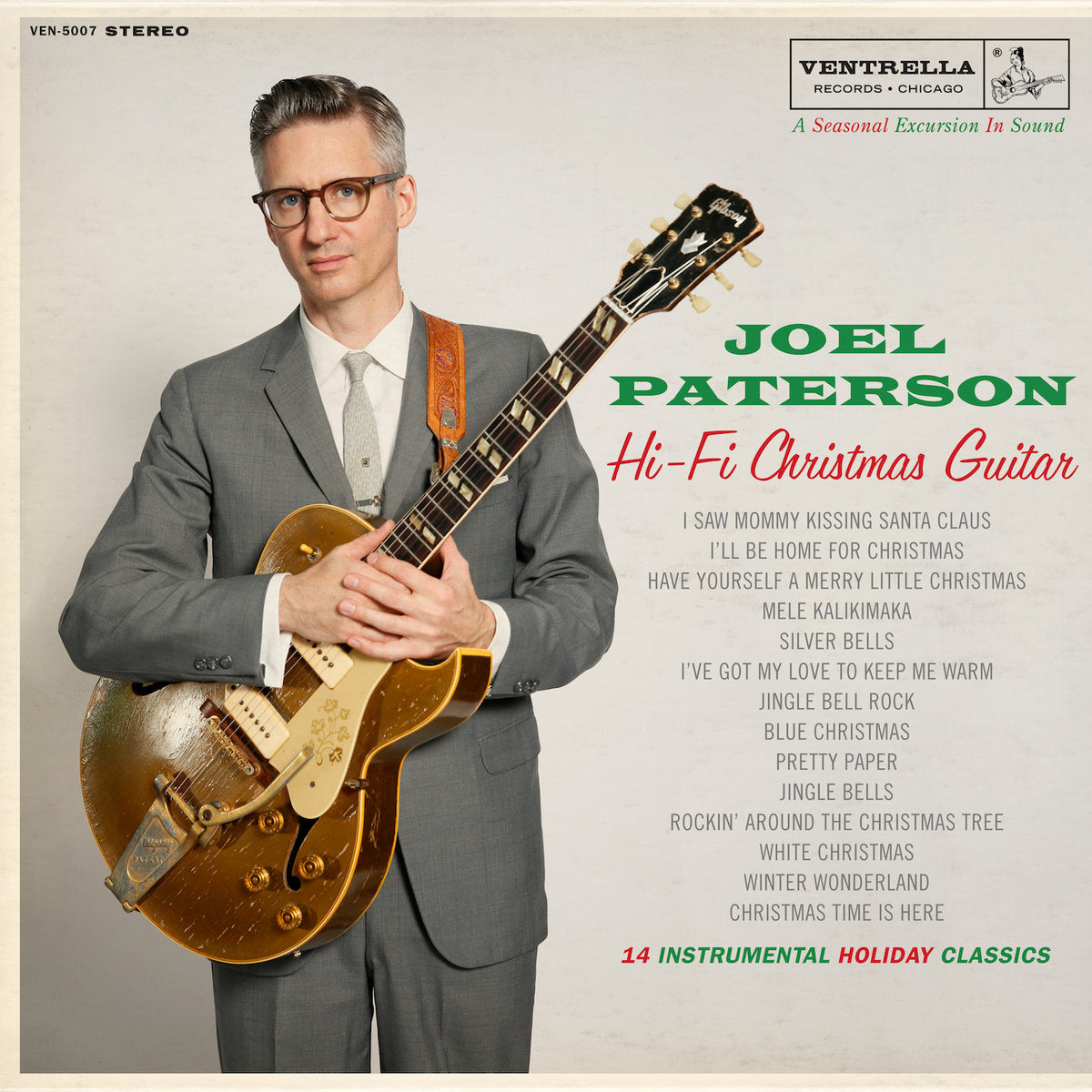 Album cover for Joel Paterson - Hi-Fi Christmas Guitar, featuring the artist in a suit, glasses, and holding a gold electric guitar, set against a textured beige background with track listings. This