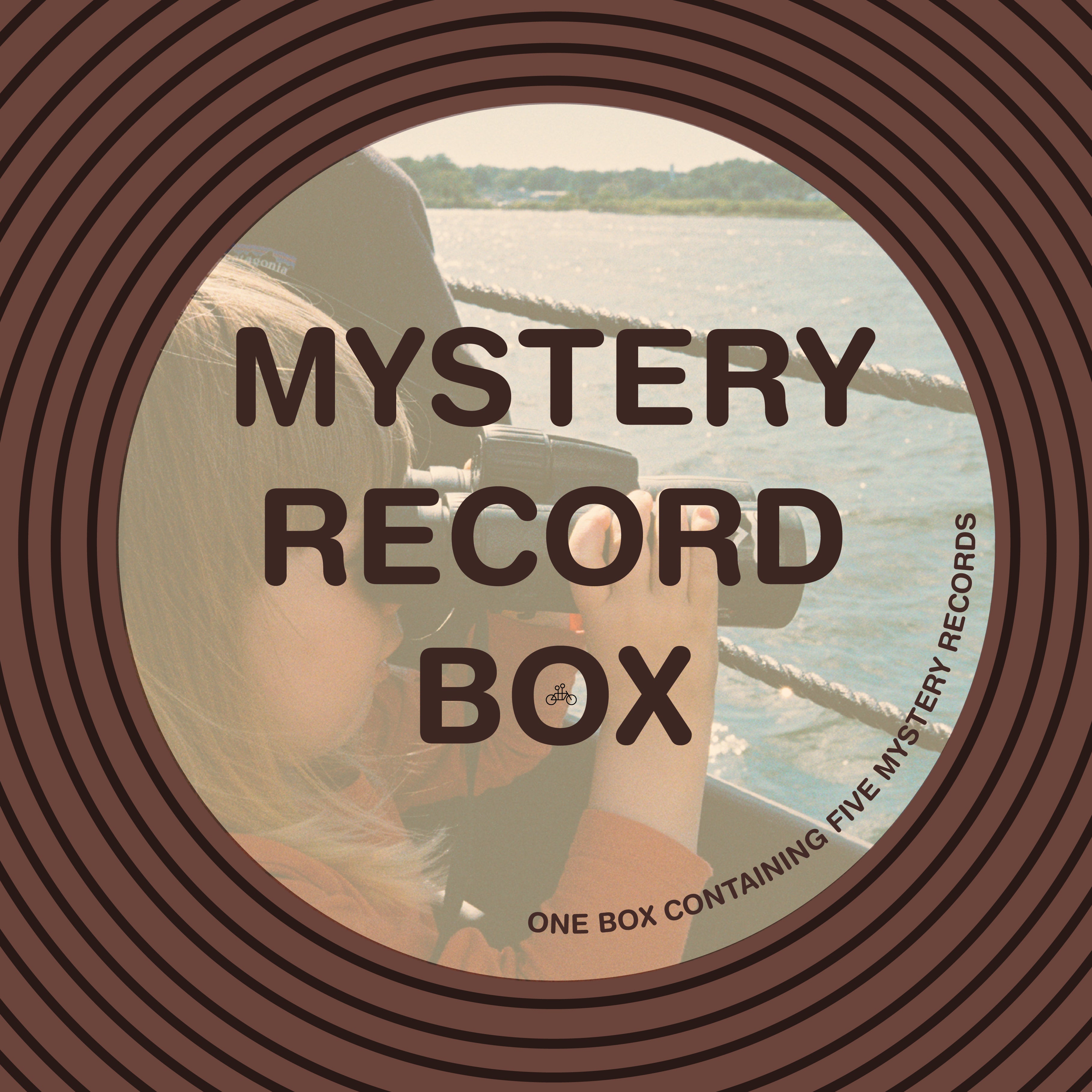 A round image shows brown concentric circles and “MYSTERY RECORD BOX” over a faded photo of a child with a camera by water. The Tandem Coffee Roasters Mystery Record Box includes five surprise vinyl records, perfect for any music lover.