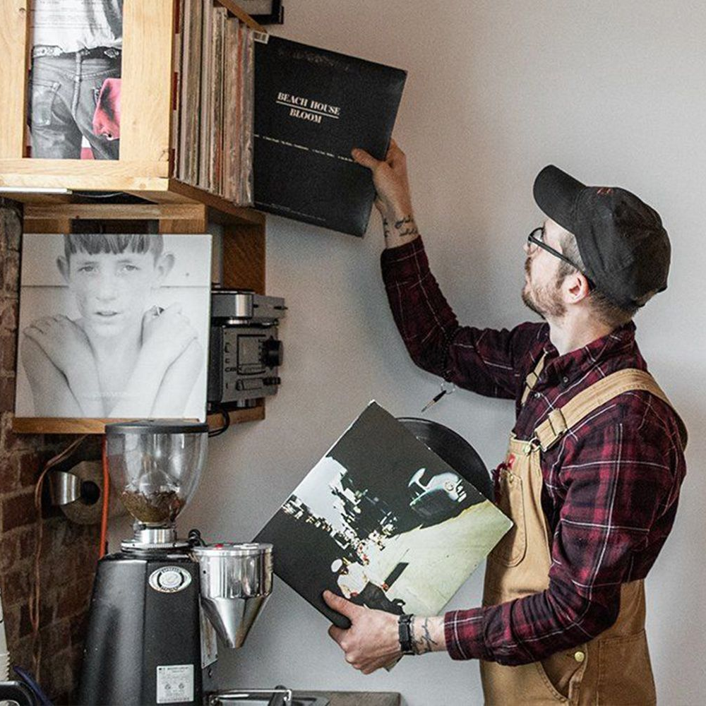 Person in a coffee shop holding vinyl records with a coffee machine in the background