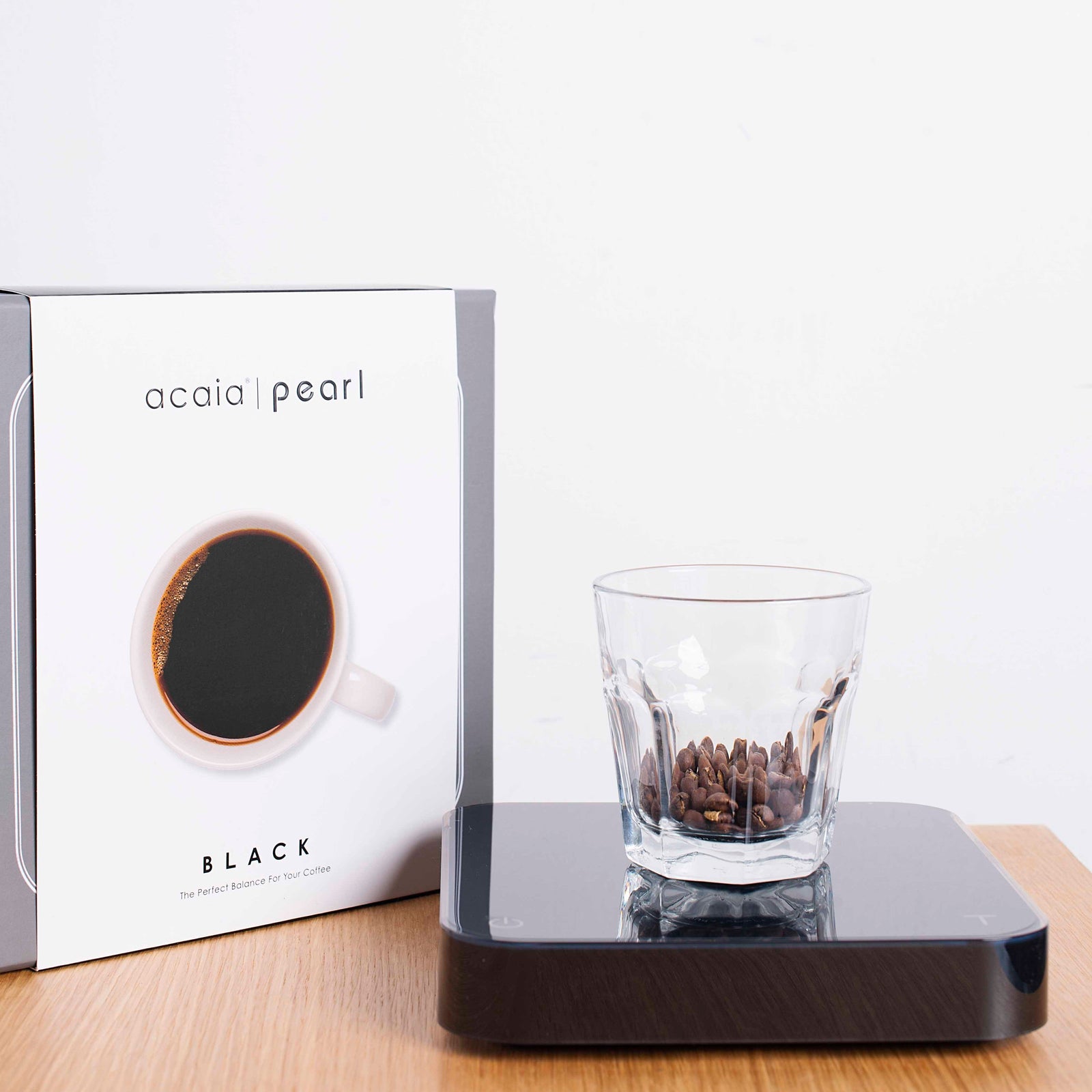 A Tandem Acaia Pearl Scale (Black) with a reflective black surface and a simple display, set against a pale yellow background. The scale shows a reading of zero and is USB rechargeable.