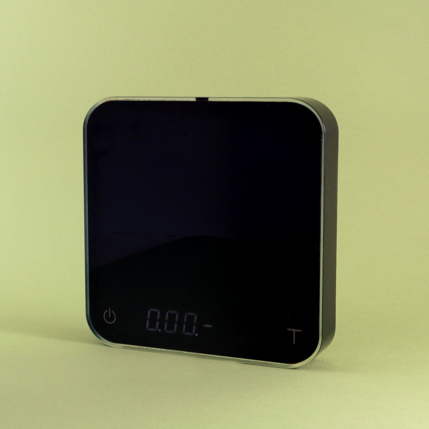 A Tandem Acaia Pearl Scale (Black) with a reflective black surface and a simple display, set against a pale yellow background. The scale shows a reading of zero and is USB rechargeable.