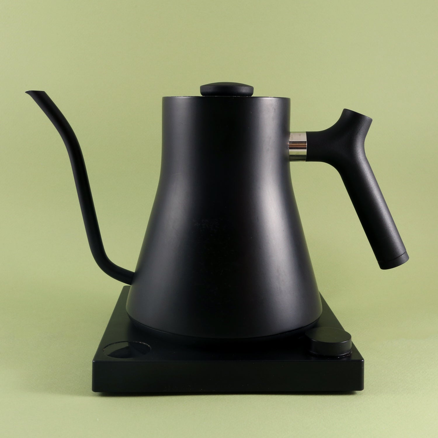 A matte black Tandem Fellow Stagg EKG electric kettle rests on its base against a soft green background.