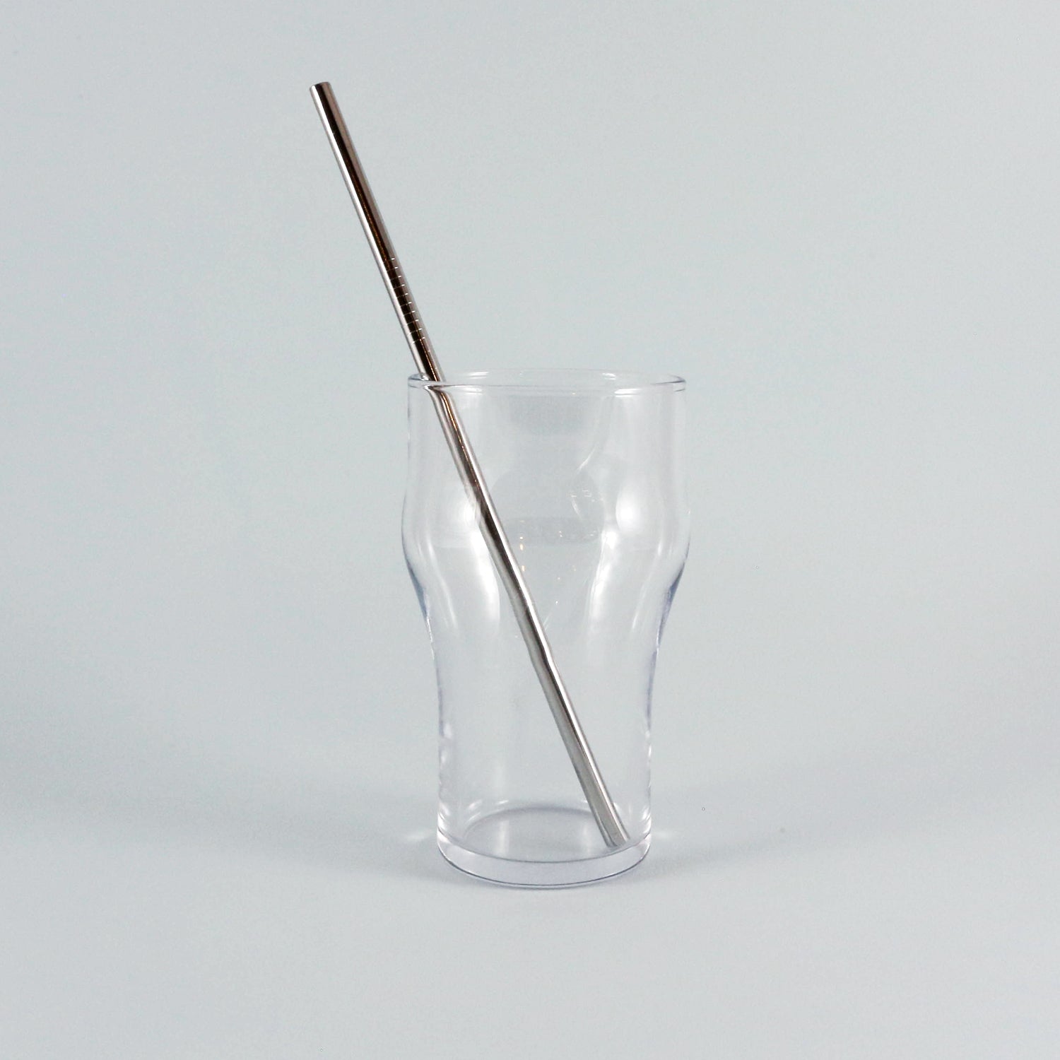 A stylish Tandem Straw from Tandem Coffee Roasters rests diagonally in an empty, clear, irregularly-shaped glass against a plain light gray background.
