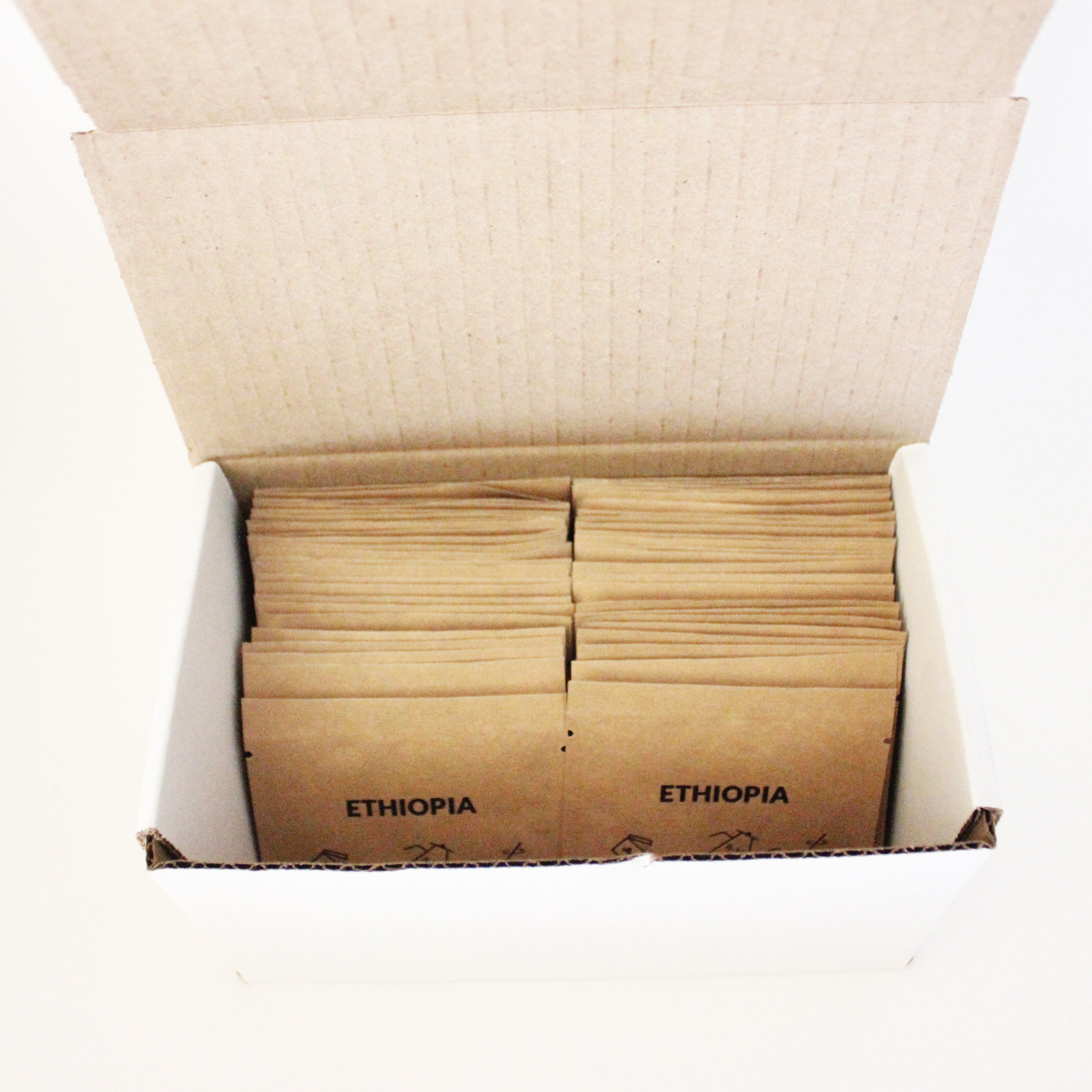 A white cardboard box is open, revealing neatly arranged brown paper packets inside. Labeled "Tandem World Voyageur" in black text, these packets of Tandem Coffee Roasters' superior coffee offer a jet-setting experience. The box is placed against a pristine white background.