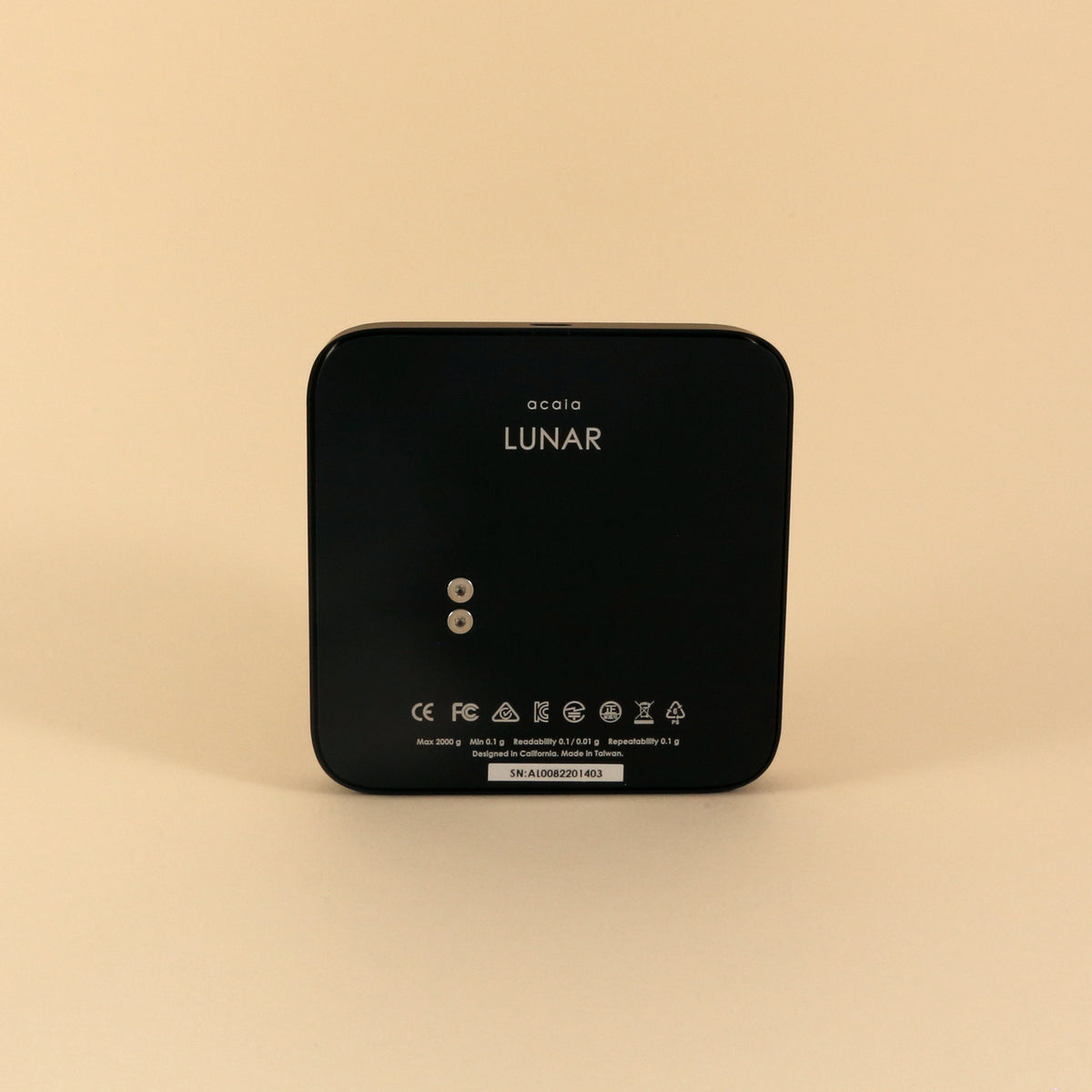 A black Tandem Acaia Lunar Scale displayed against a beige background, featuring digital controls and high accuracy with minimalistic design and product markings.