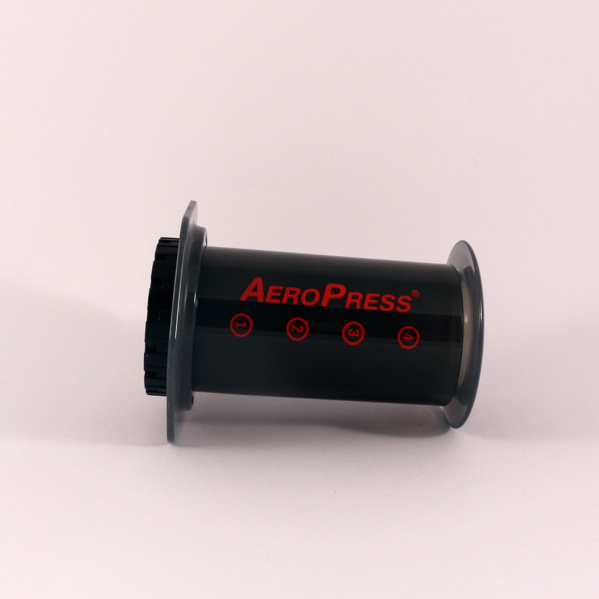 A Tandem Aeropress chamber with red text and symbols, positioned upright against a plain light background.