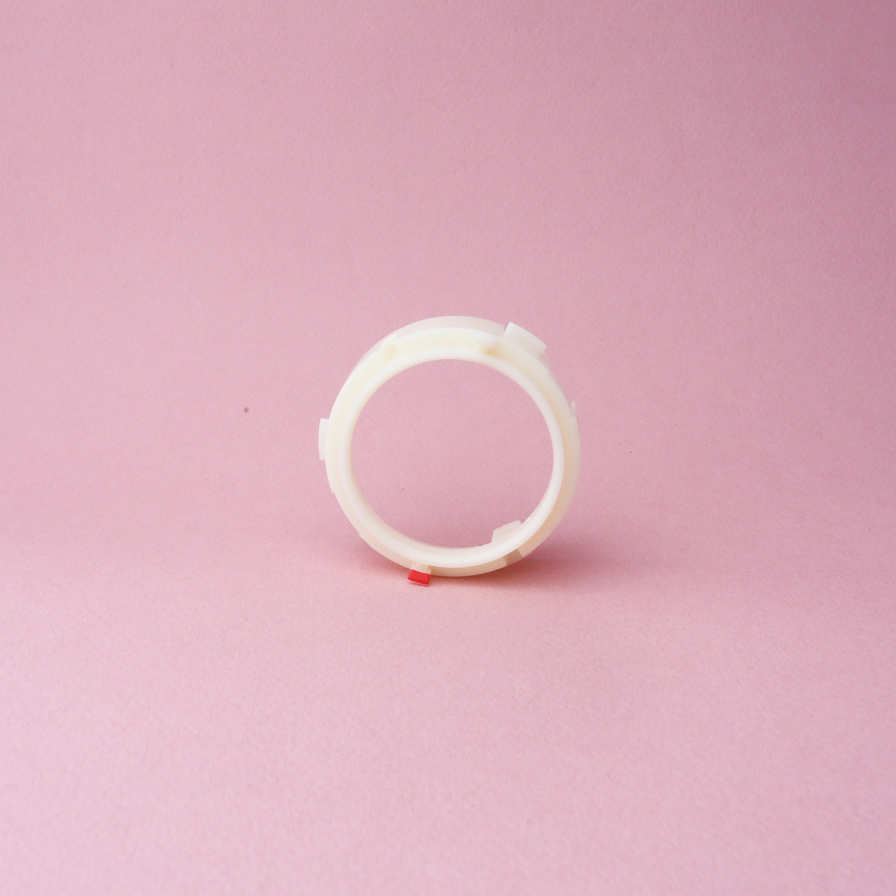 A white plastic Baratza Ring Burr Holder by Tandem Coffee Roasters, featuring a small red tab, stands upright on a pink background.