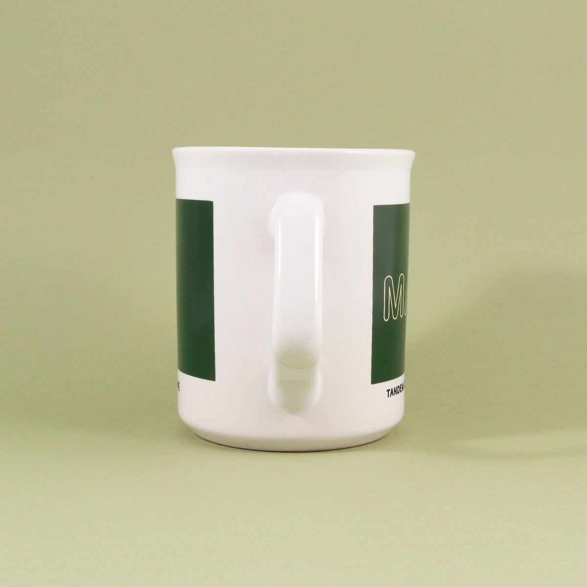 White ceramic 11oz Maine Mug from Tandem Coffee Roasters with green vertical stripes and an embossed handle, featuring a minimalist design and a small logo on a light green background.