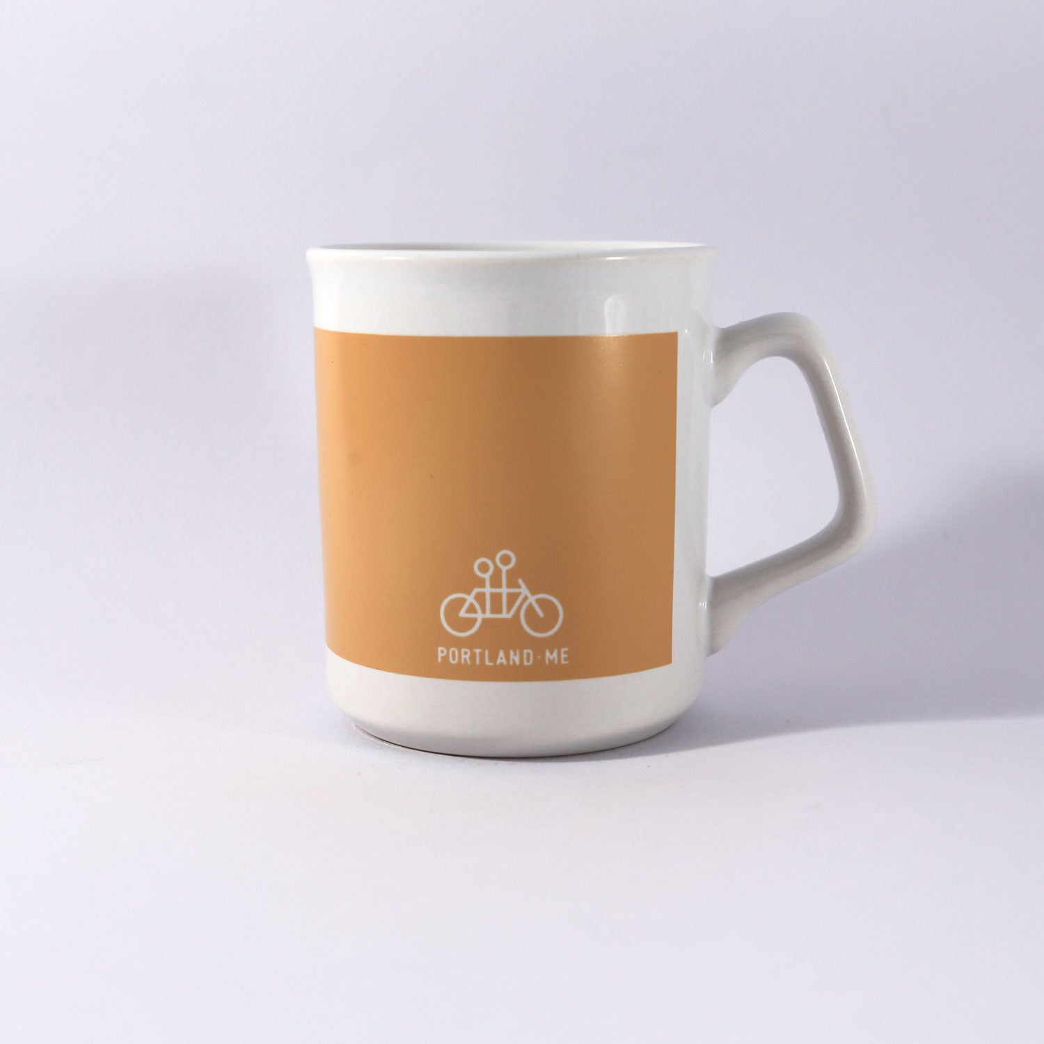 A white ceramic mug with a beige center band featuring the text "Kathy Heideman Spread Joy Mug" in a black square frame on a plain background, recommended for handwash only. Made by Tandem Coffee Roasters.