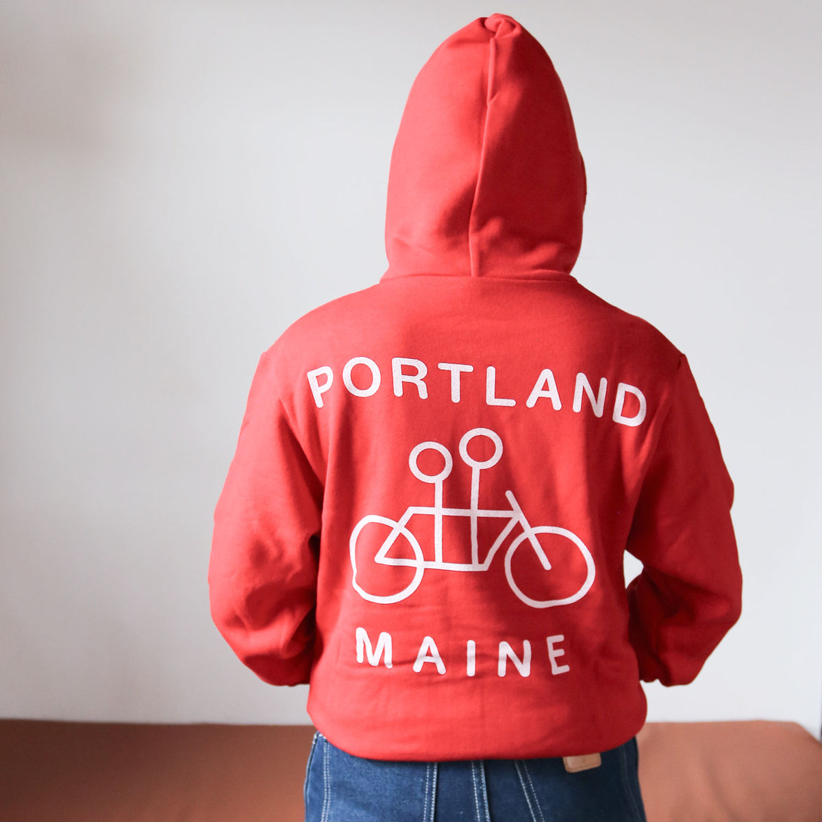 Person from behind wearing a Tandem Coffee Roasters red zip-up hoodie with "Portland Maine" text and a bicycle graphic, standing against a neutral background.