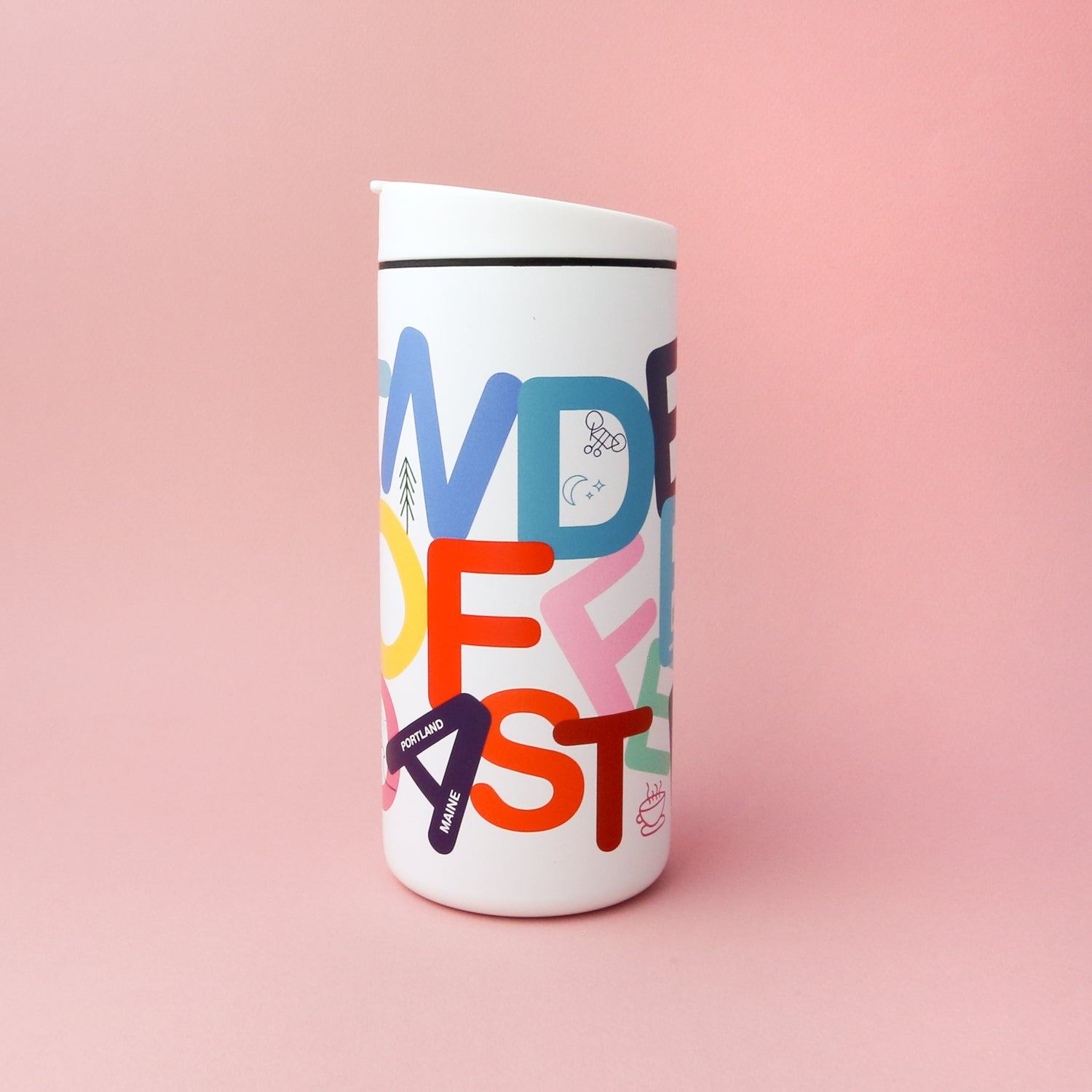 A white travel mug with a colorful design featuring large, overlapping letters and small illustrations. The letters spell out "WONDER FEST" in red, yellow, purple, green, and blue on a light pink background. The Tandem Coffee Roasters Letter Mug also comes with a leak-proof lid for convenience.