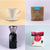 A collage of four images: a white ceramic Tandem Coffee Roasters V60 Starter Kit coffee dripper, a bag of freshly roasted La Piramide coffee beans, a black coffee grinder, and a pack of coffee filters.