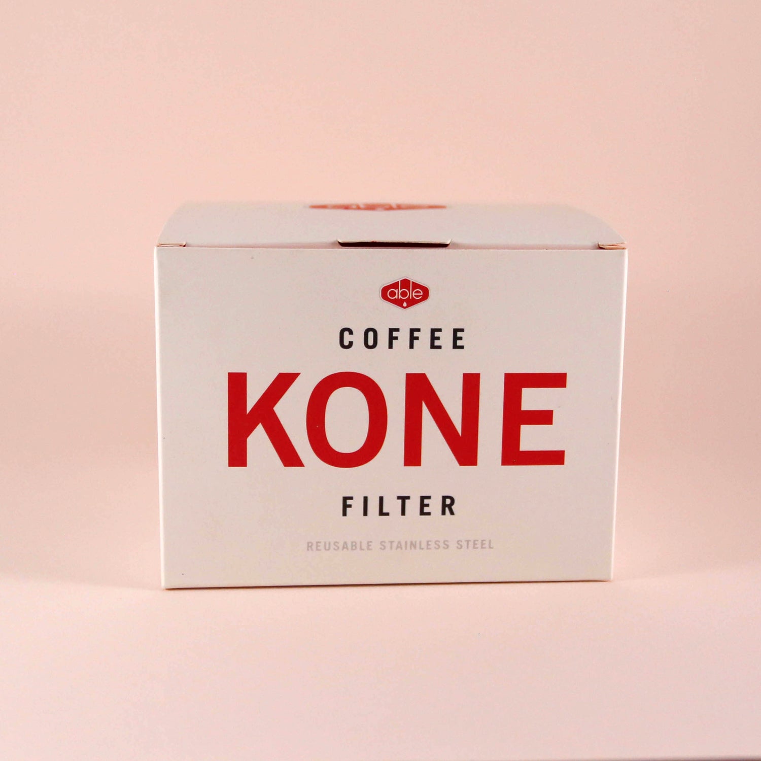 A Tandem Coffee Roasters Able Coffee Kone stainless steel reusable coffee filter next to its packaging box on a light pink background. The box displays the product name prominently.