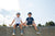 Two young boys wearing helmets and Tandem Kids Tandem Sun tees sit on the edge of a skateboard ramp under a clear blue sky, smiling and looking relaxed.