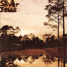 Album cover for "Starlite Walker" by Silver Jews depicting a serene sunset over a still lake surrounded by dense trees, reflecting a warm sky and silhouettes of trees on water.