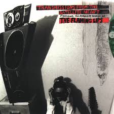 Album cover of "The Flaming Lips - Transmission from the Satellite Heart" by Tandem Coffee Roasters, featuring a man hunched over photographic equipment with cameras and film, set against a surreal backdrop with a giant footprint.